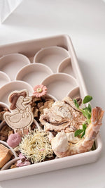 Decorative freeze dried prawn and freeze dried Octopus including a chicken figurine, flowers, and shrimp in a dogged fish scale slow feeder on a white background