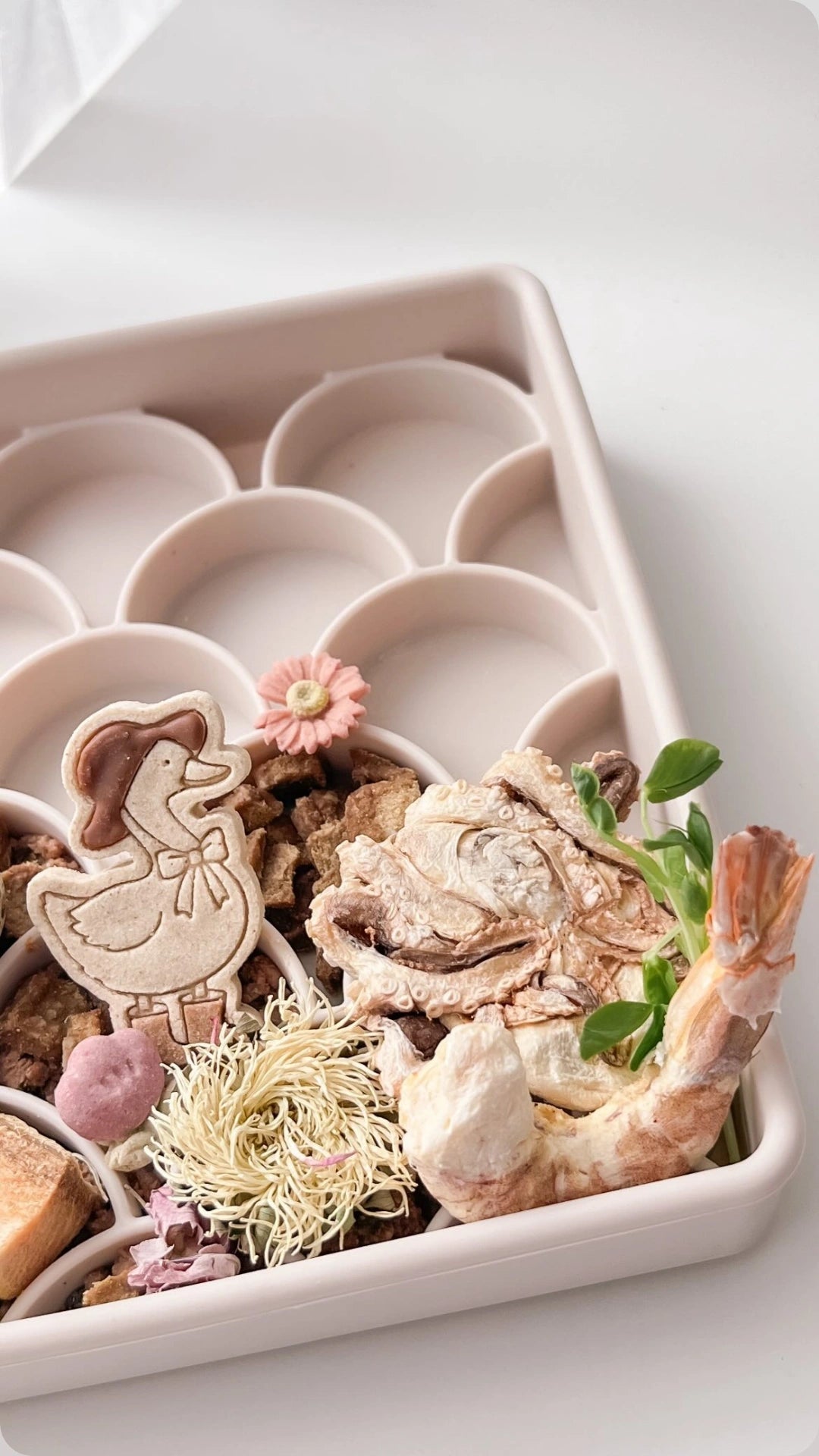 Decorative freeze dried prawn and freeze dried Octopus including a chicken figurine, flowers, and shrimp in a dogged fish scale slow feeder on a white background