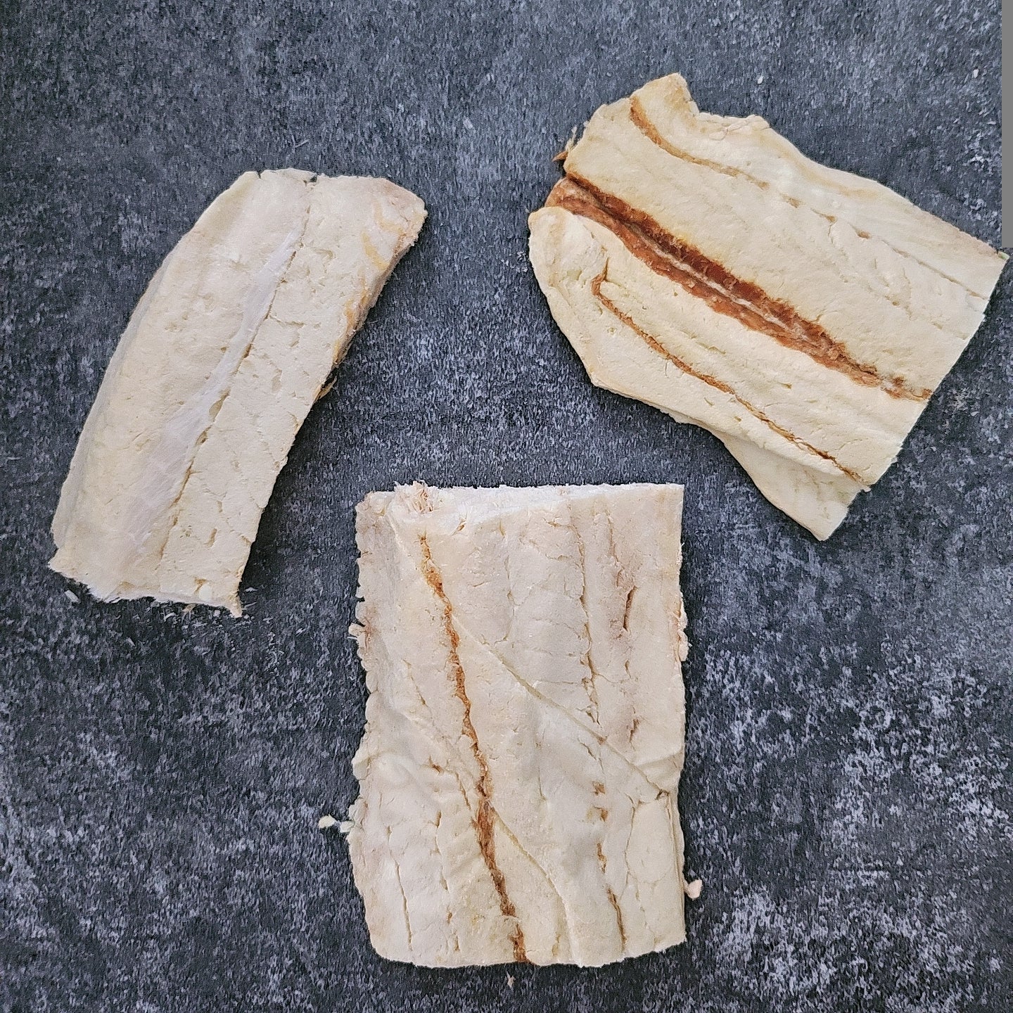 Three pieces of freeze dried Hoki fillets on a dark textured surface
