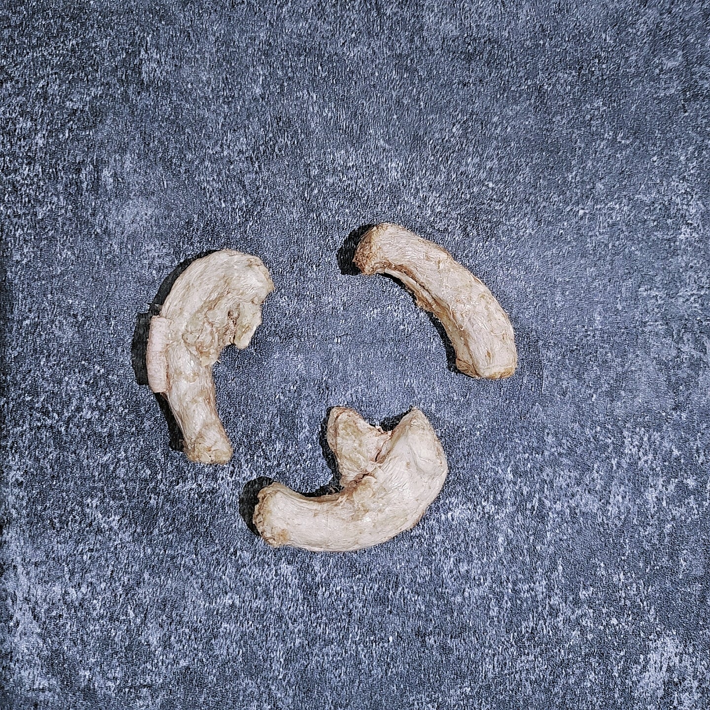 Three pieces of dried quail necks on a textured gray surface